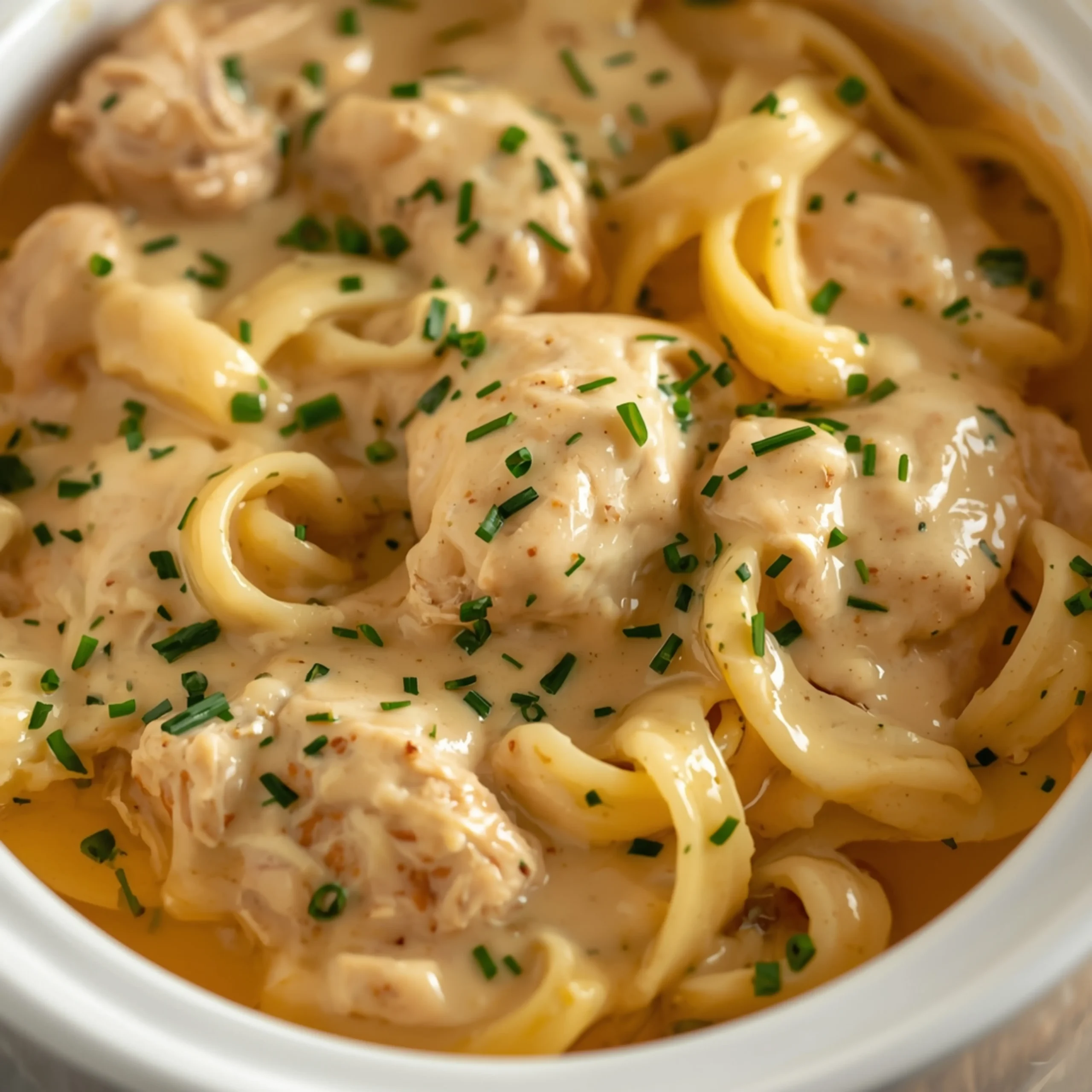 Close-up of Crockpot Chicken Alfredo cooked in a Crockpot with fresh herbs and glossy sauce